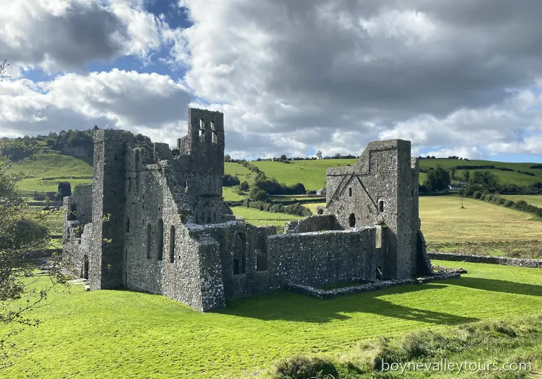 Stone ruins of Fore Abbey standing in a green field under a cloudy sky.