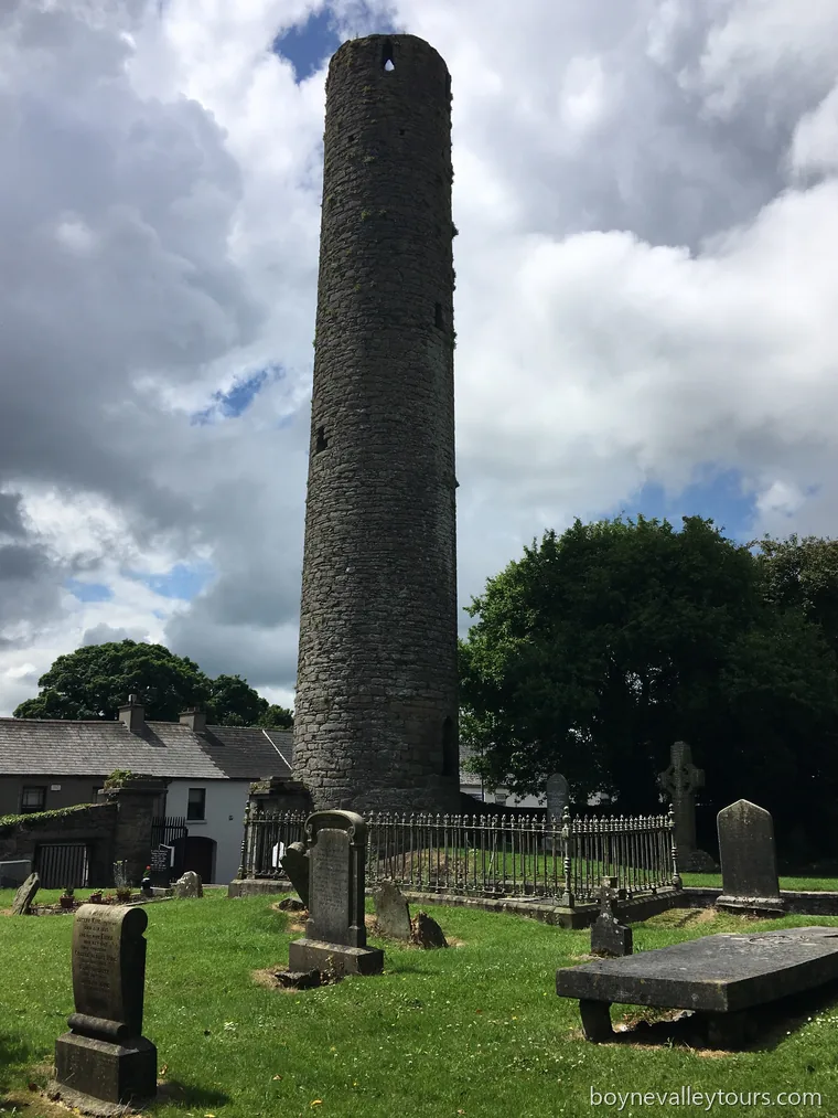 Kells Round Tower rising above the churchyard, with gravestones and cloudy sky.